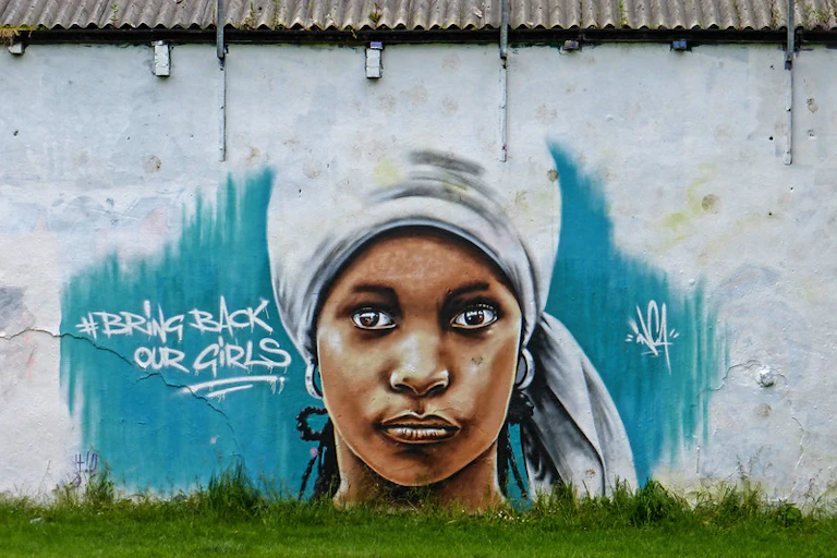 A mural of a young woman in a head wrap, eyes gazing intently, painted on a wall.