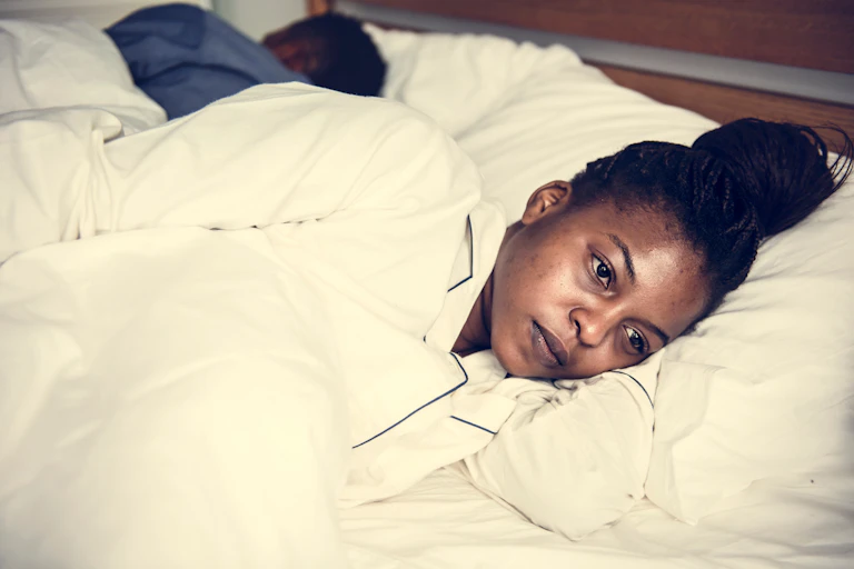 a woman lies in bed turned away from her spous