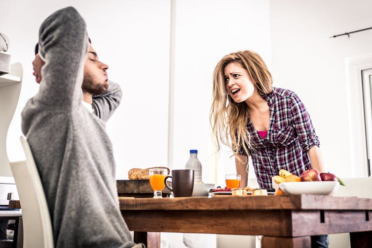 a woman yells across a table at a man with his hands behind his head