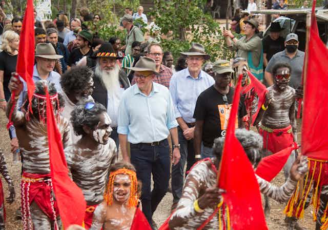 Anthony Albanese walking with a crowd carrying red flags and Yothu Yindi board member Djaawa Yunupingu during the Garma Festival in northeast Arnhem Land.