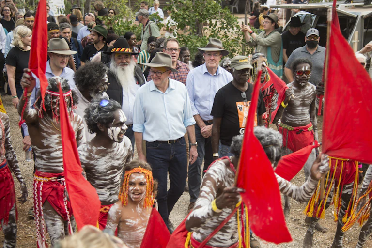Anthony Albanese walking with a crowd carrying red flags and Yothu Yindi board member Djaawa Yunupingu during the Garma Festival in northeast Arnhem Land.