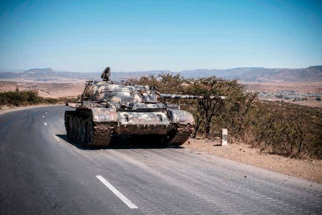 A military tank occupying one lane of a two-lane tarmac road.