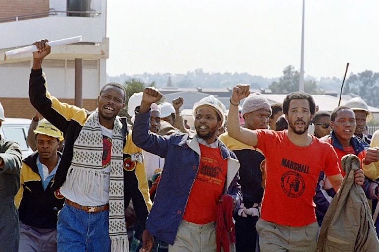 Men wearing trade union T-shirts raise clenched fists while singing.