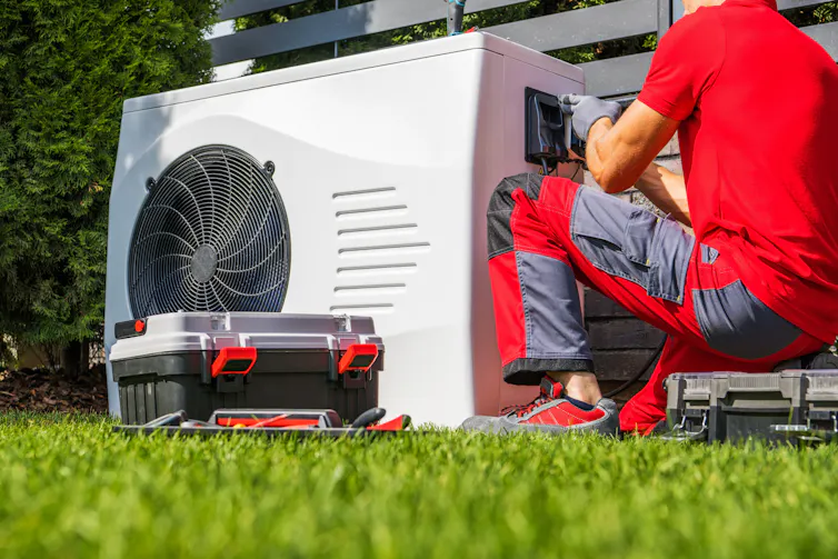 An engineer in red uniform tweaks a large, white unit with an in-built fan.