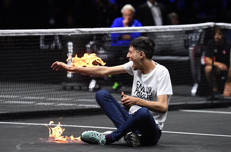 Man on tennis court with his arm on fire.
