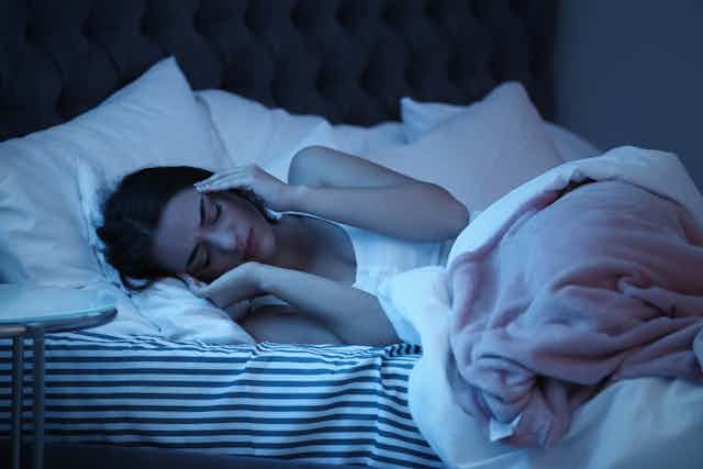 Una mujer tumbada en la cama de noche se lleva las manos a las sienes.