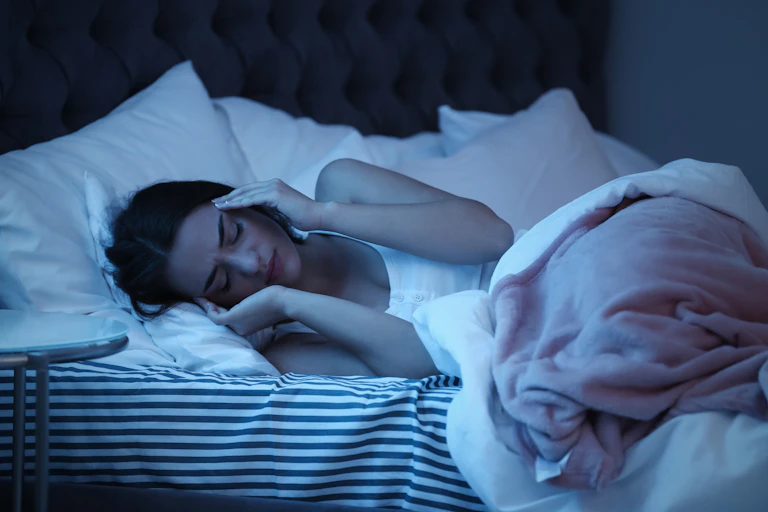 Una mujer tumbada en la cama de noche se lleva las manos a las sienes.