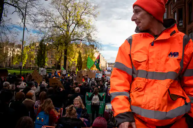 A man in a high-visibility jacket looks on as a climate march passes.