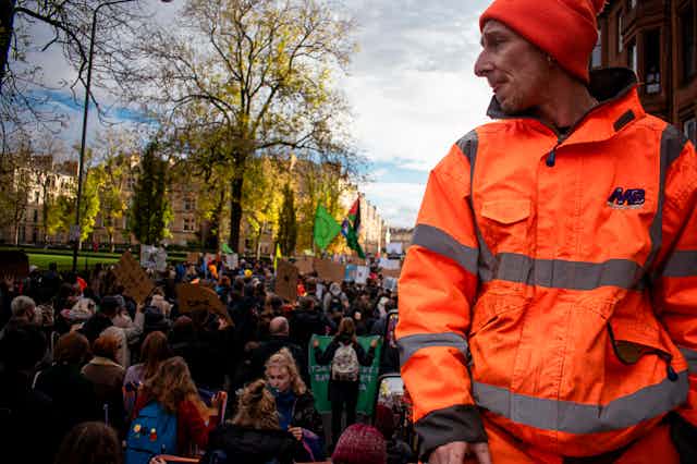 A man in a high-visibility jacket looks on as a climate march passes.
