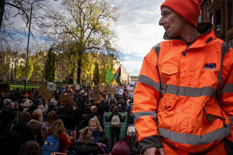 A man in a high-visibility jacket looks on as a climate march passes.