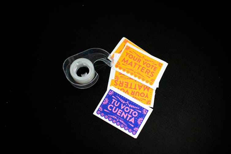 A roll of tape on a black table next three cards which say 'Your vote matters' and 'Tu voto cuenta.'