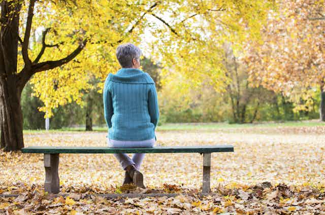 Woman sits on park bench in Autumn