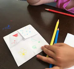 Pencil crayons seen laying overtop of folded paper with designs.