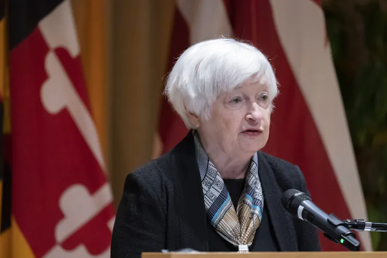 An elderly woman in a blazer speaking into a microphone from behind a podium