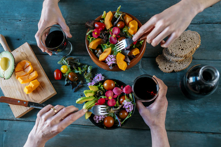 Top view of a table with two people eating bowls of healthy, colorful mixed salads.
