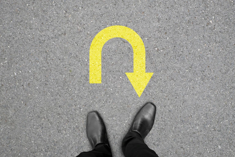 Two feet, black dress shoes, yellow U-turn arrow on tarmac.