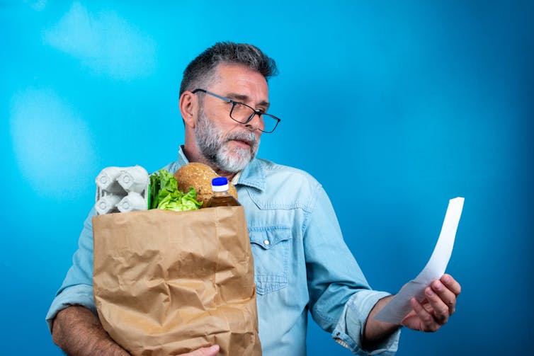 Man with beard & groceries in a brown paper bag, receipt, glasses.