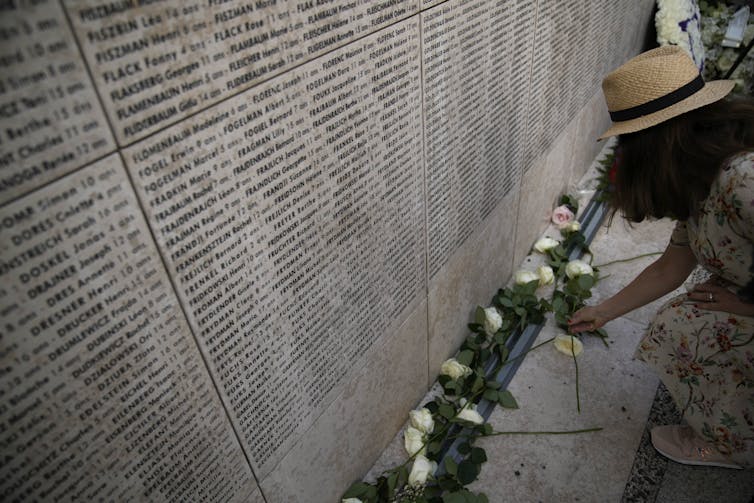 A woman seen standing at the side of a wall of names.