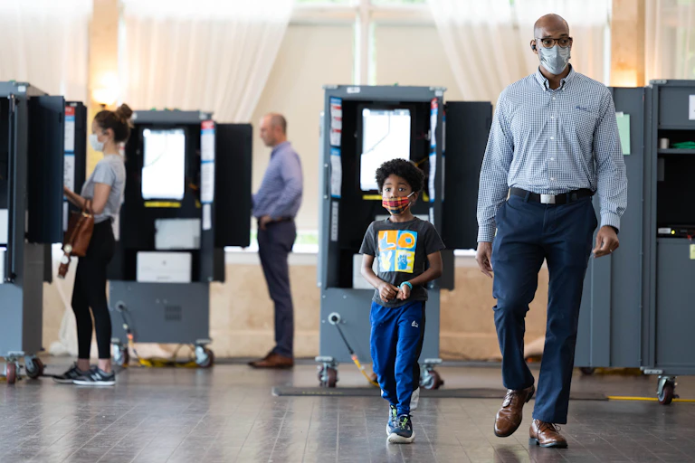 A black man is walking with his son as they leave a polling station after casting a ballot.