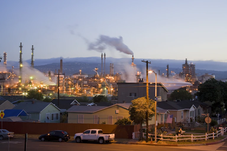 Modest houses sit adjacent to an oil refinery venting pollution out of smoke stacks