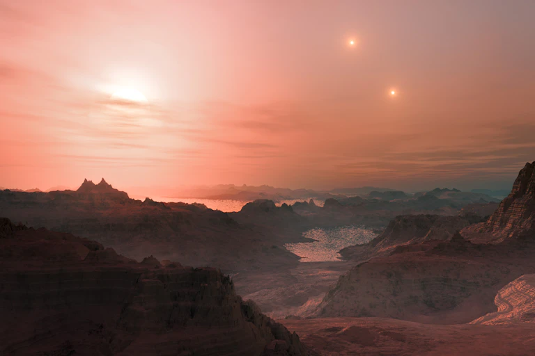 Artist impression of a mountainous landscape with a lake and possibly an ocean just before the horizon. One sun is just setting, but two other suns still appear in the sky. The sky is hazy and the sunset has turned it red.