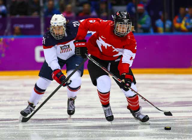 Two women in hockey gear on an ice rink.