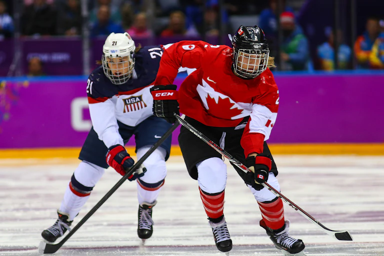 Two women in hockey gear on an ice rink.