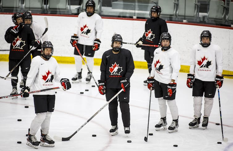 Members of Canada's women's hockey team wearing hockey gear standing on an ice rink.