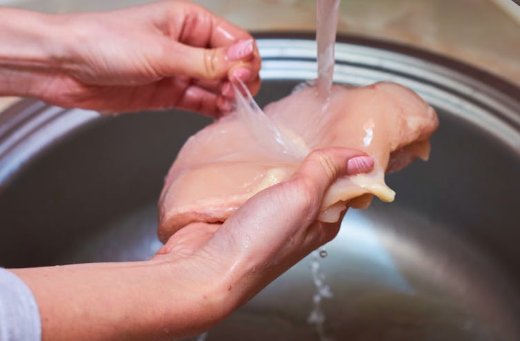 A person washes chicken over a sink.