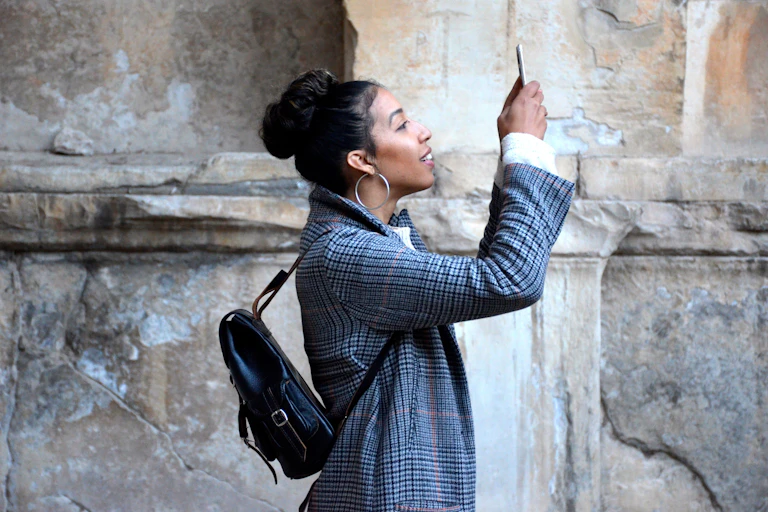 A woman with dark hair in a blazer taking a selfie in front of a sandstone wall