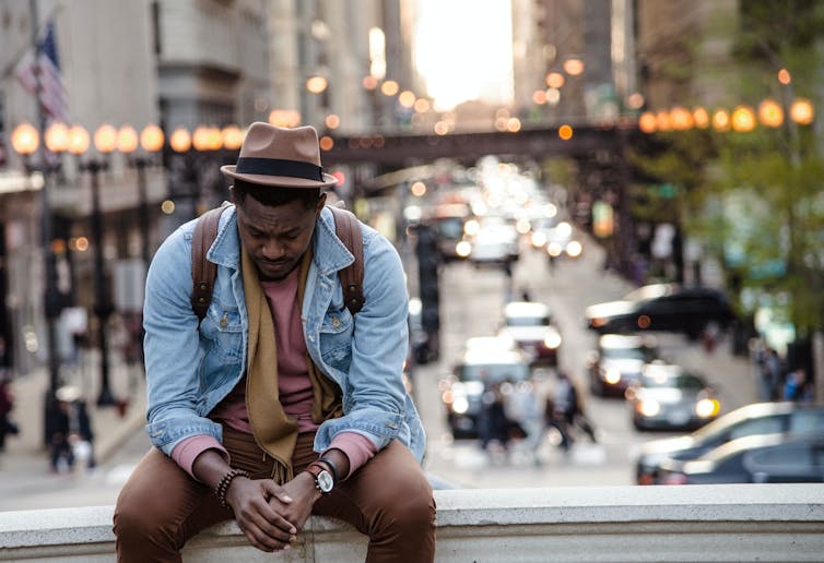 Man sits on a ledge over a busy street