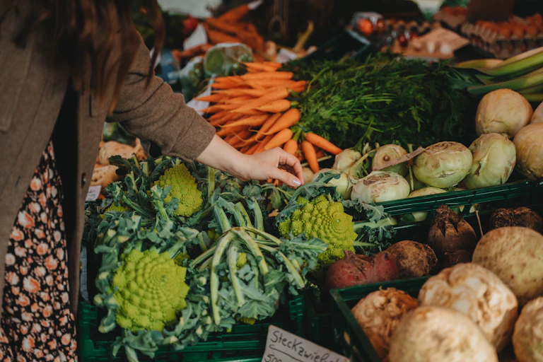 A woman reaches for vegetables at a stall.