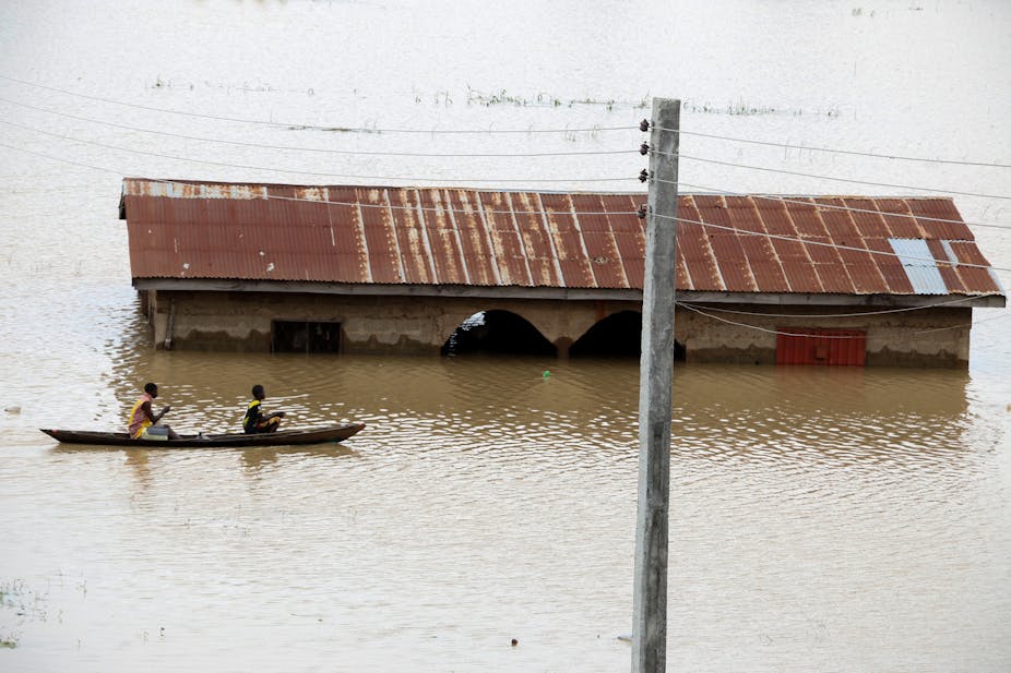 Men steer a dugout canoe past a flooded house following heavy rain in the Nigerian town of Lokoja, in Kogi State.