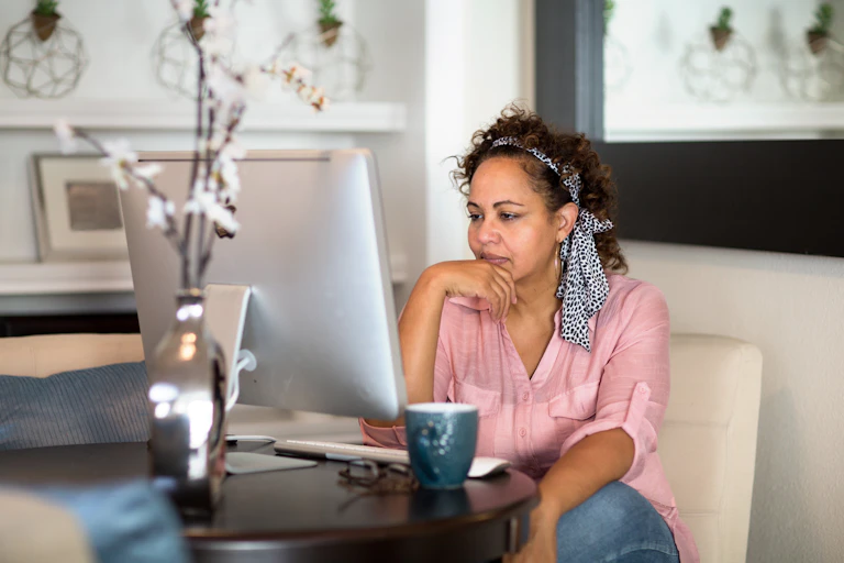 Woman at computer, mug, pink shirt, hair tie.