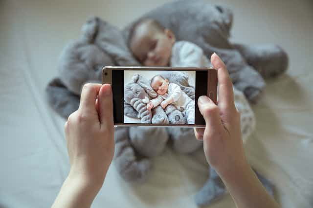 Hands taking photo of sleeping baby on mobile phone
