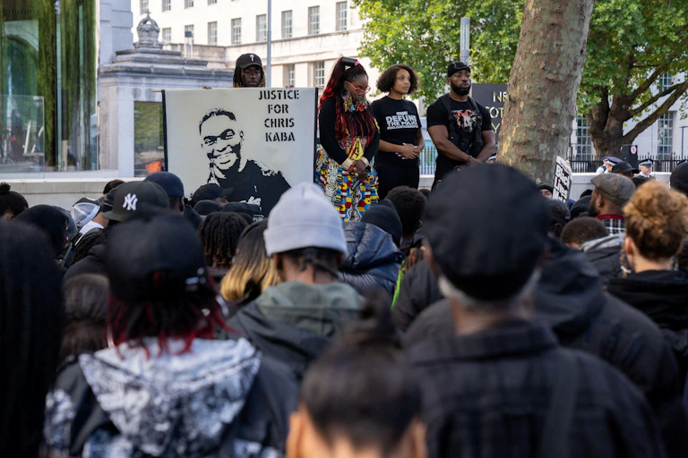 Protestors stand heads bowed in a public square.