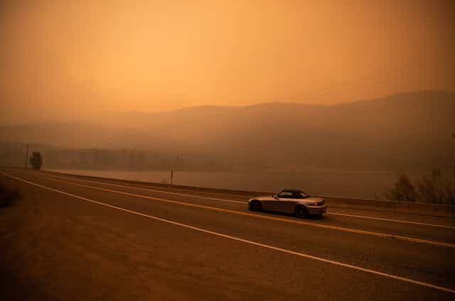a lone car drives down a highway through a reddish mist