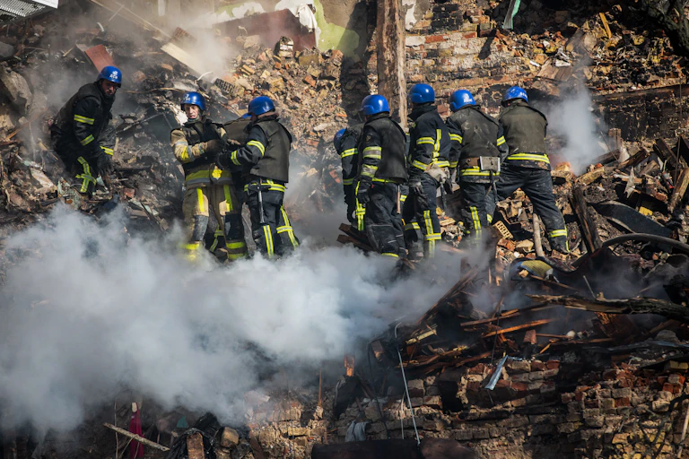 Workers in black and yellow uniforms and blue helmets work on a rubble-filled site.