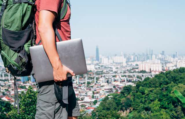 Man with laptop and backpack above city skyline.