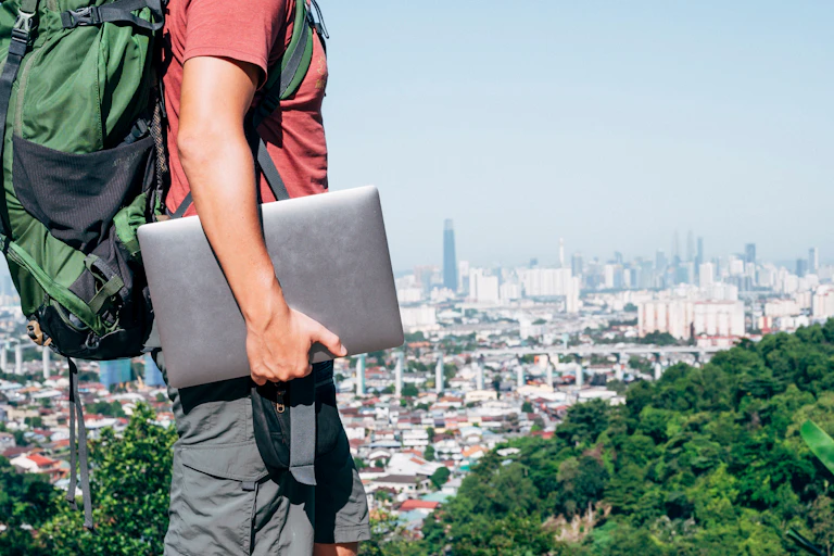 Man with laptop and backpack above city skyline.