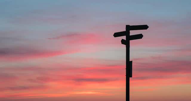 A road sign post is seen against a pink sky.