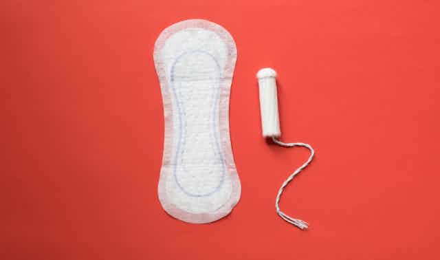 A sanitary pad and tampon, both unwrapped and unused, on a bright red background