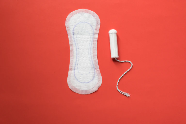 A sanitary pad and tampon, both unwrapped and unused, on a bright red background