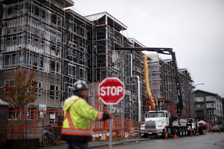 A construction worker holds a stop sign outside a building under construction.