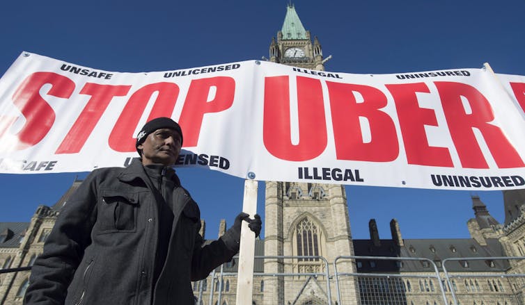 A man stands in front of a banner that reads Stop Uber in front of the Peace Tower.