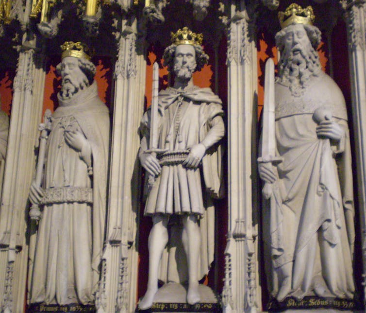 Three marble statues of men wearing robes and crowns appear side by side.