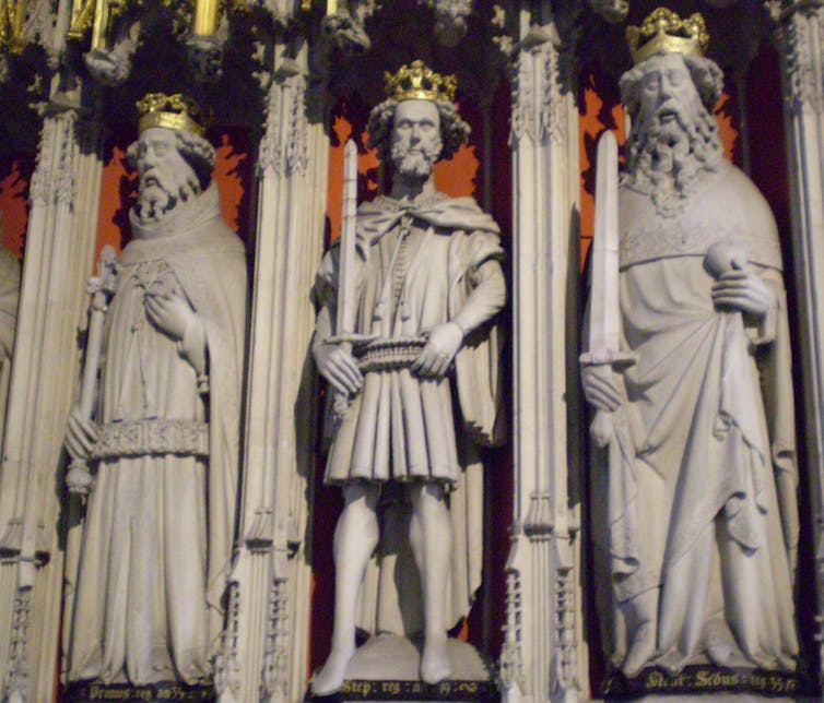 Three marble statues of men wearing robes and crowns appear side by side.