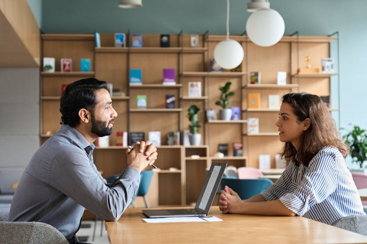 A man and a woman sit across from each other at a conference table in an office