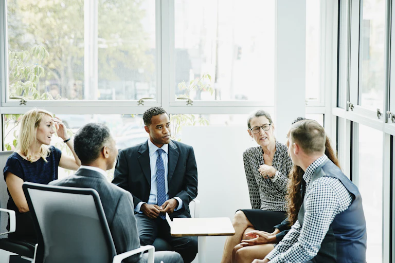 A diverse group of people gather in a sunny office