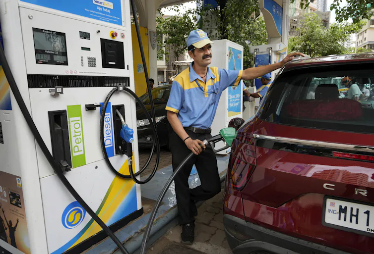 A man in a blue and yellow polo shirt fills a car with gas at a gas station